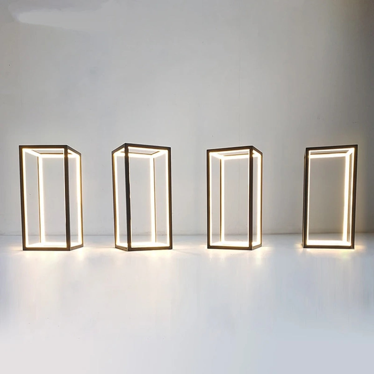 Four Welion wireframe table lamps glowing warm, showing the open rectangular prism design from different angles