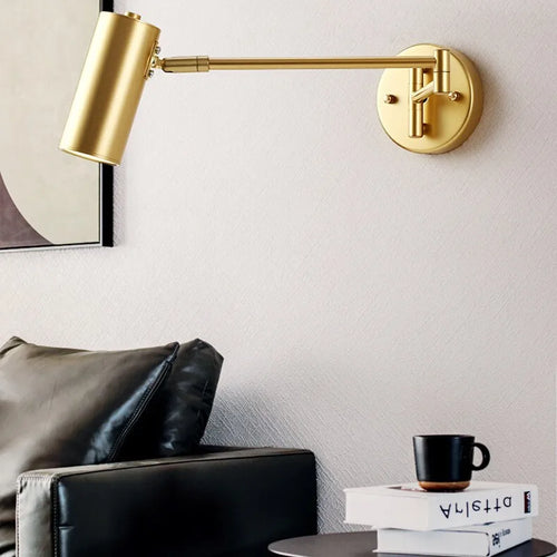 Arqventa brushed gold swing-arm wall sconce beside a black leather sofa