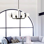 Noctivox chandelier in matte black beneath an arched window, above a grey sofa