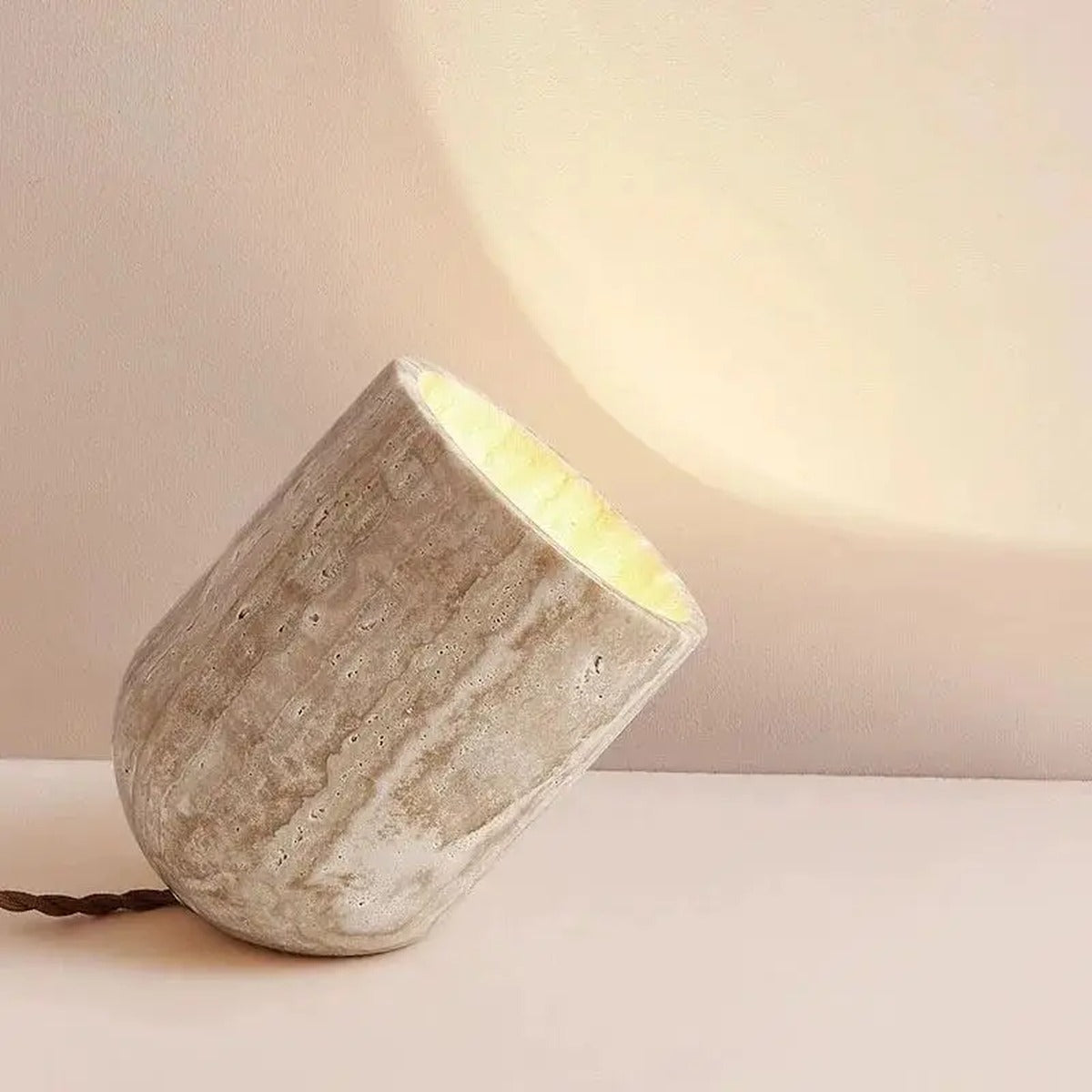 Farlux organic travertine stone column table lamp — rough cylindrical stone with warm upward glow on wall