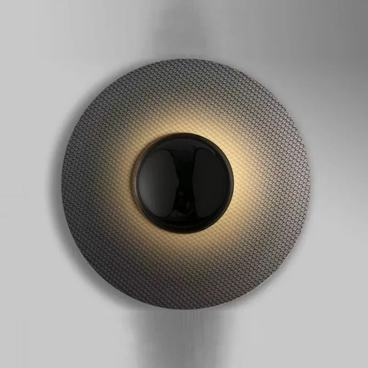 Larleon woven mesh disc halo wall sconce — dark textured disc with glossy black center sphere and warm radial LED gradient on grey wall