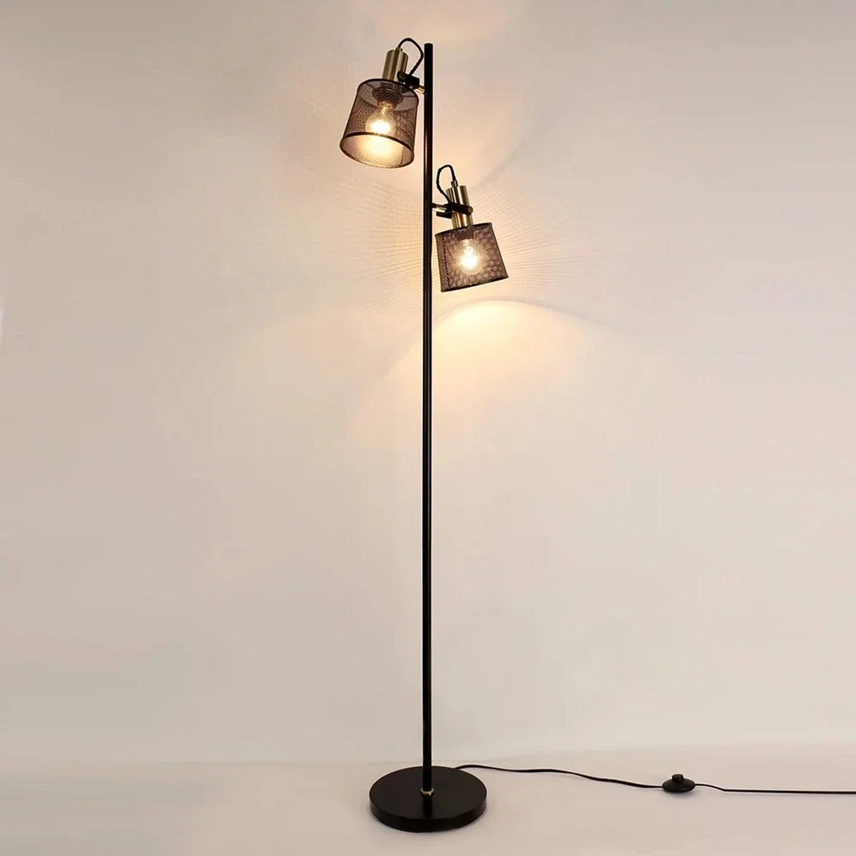 Pivotis floor lamp with two brass-hinged mesh shade heads, both illuminated