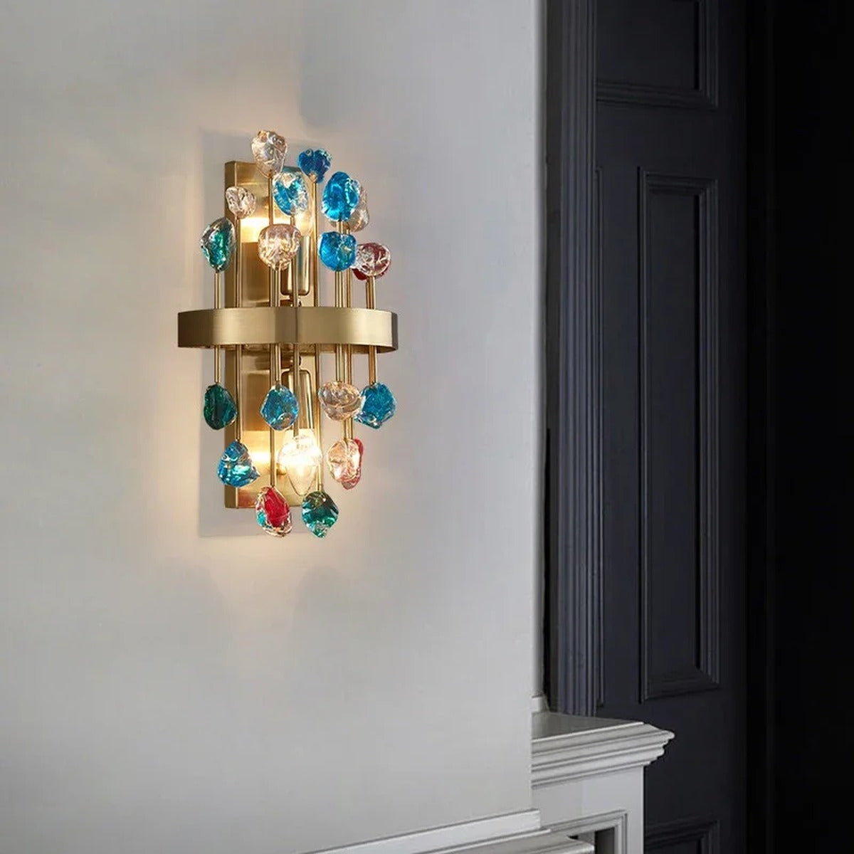 Morvena crystal cluster wall sconce in Rainbow Gemstone Crystal, brushed brass frame, lit in a hallway