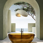 Tempero organic stone-texture dome pendant in stone grey, glowing warm above a sculptural bathtub with sea view