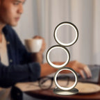 Circolia triple ring LED table lamp in Matte Black, glowing warm white in a home office setting
