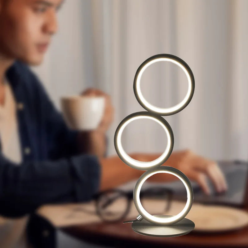 Circolia triple ring LED table lamp in Matte Black, glowing warm white in a home office setting