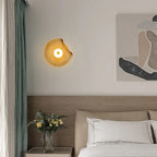 Devoria organic wavy frosted glass wall sconce in amber, glowing warmly beside a bed in a minimalist bedroom
