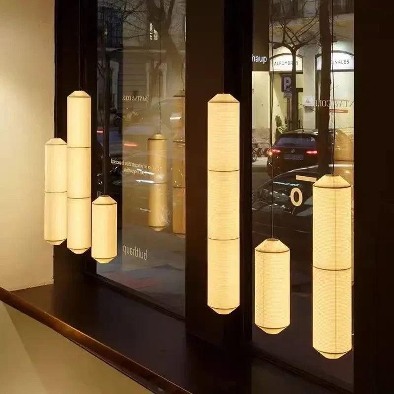 Shizumi paper drum pendant lights in varying heights, illuminated storefront at night