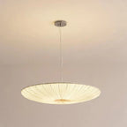 Fornox pleated fabric saucer light illuminated above a bed in a soft neutral bedroom