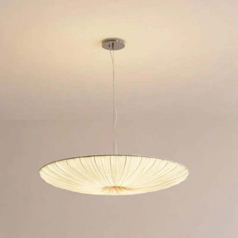 Fornox pleated fabric saucer light illuminated above a bed in a soft neutral bedroom