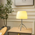 Mouth-blown glass tripod table lamp, White shade, chrome base, lit on a bedside table