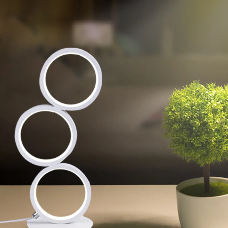 Circolia triple ring LED table lamp in Pure White on a shelf next to a potted plant