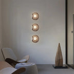 Three Devoria wall sconces in smoky grey mounted in a vertical column beside a lounge chair