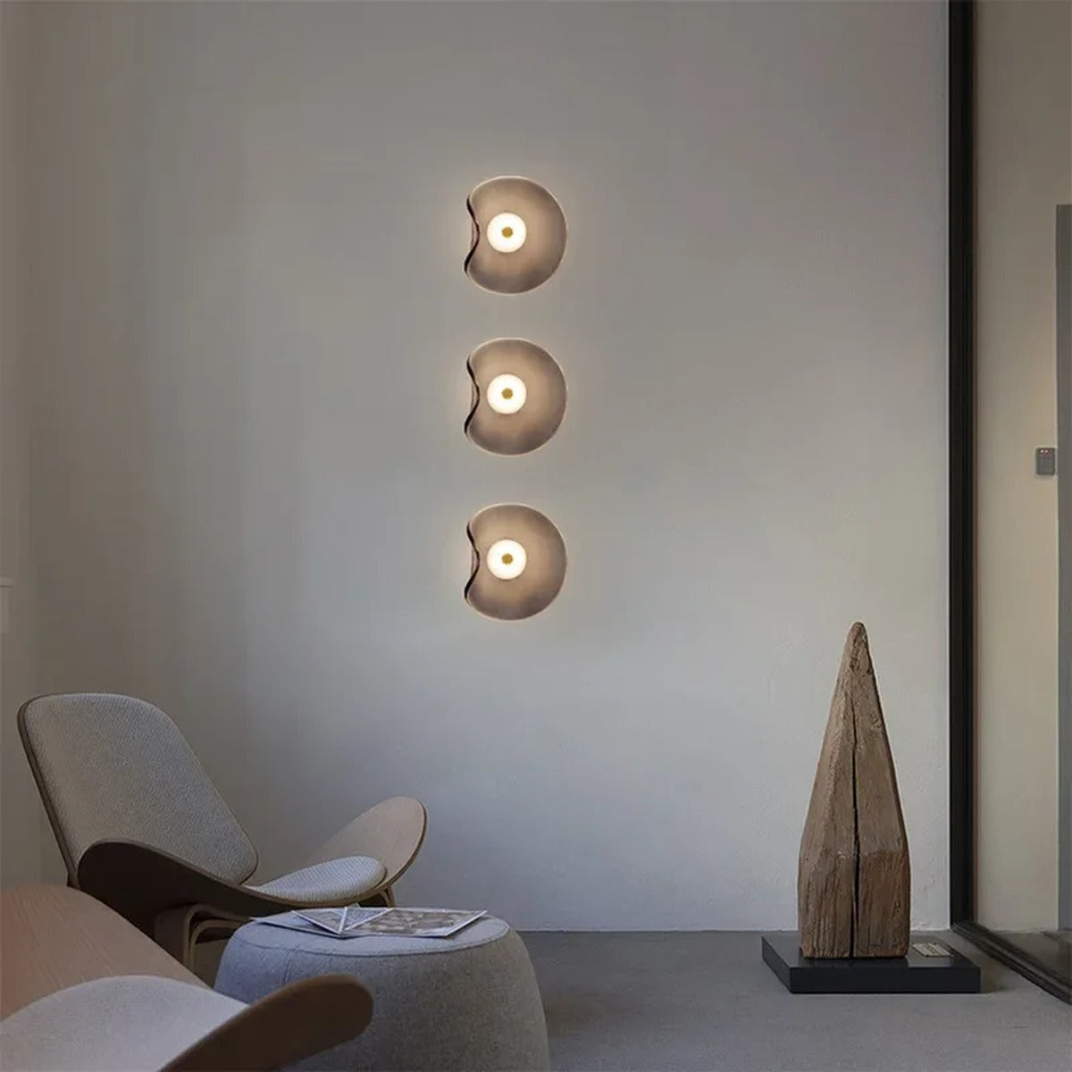 Three Devoria wall sconces in smoky grey mounted in a vertical column beside a lounge chair
