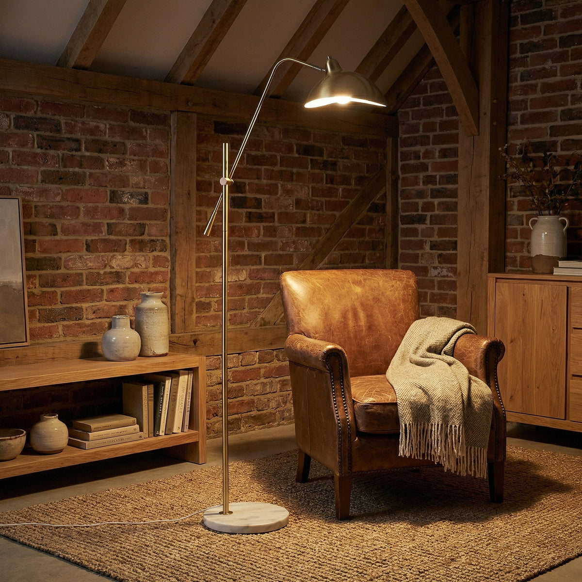 Aurevon gold floor lamp illuminating a cozy reading corner beside a leather armchair