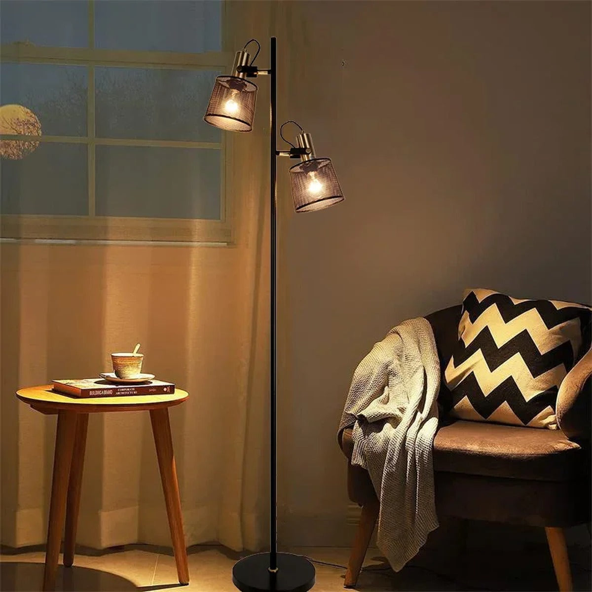 Pivotis dual-arm floor lamp beside a reading chair, warm mesh-shade light in a living room
