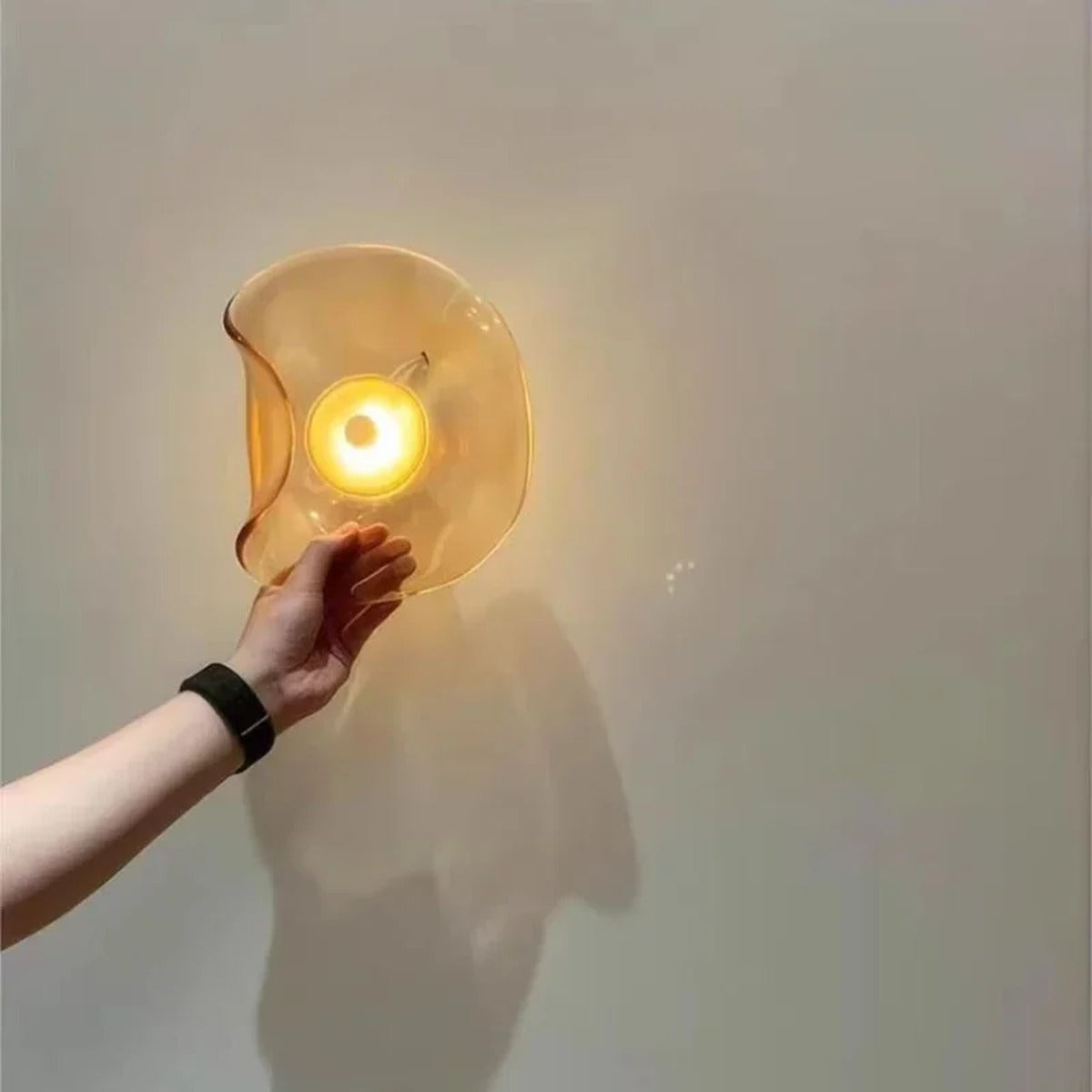 Hand holding the Devoria wall sconce lit in amber, showing its scale and the folded edge of the glass