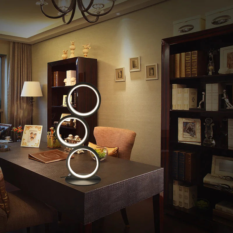 Circolia triple ring LED table lamp in Matte Black on a desk in a furnished study