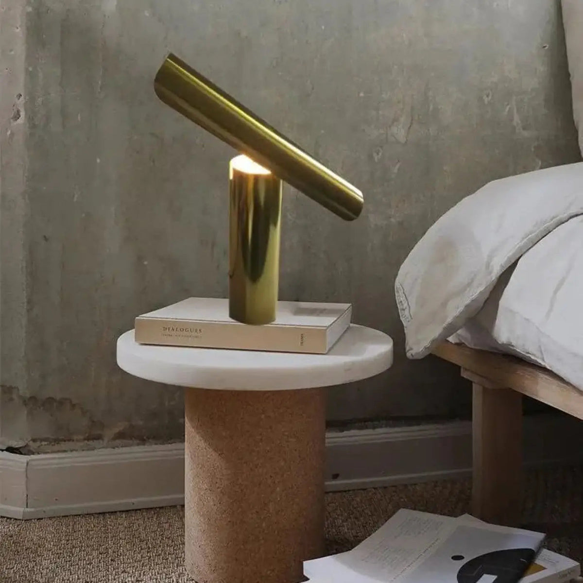Izora inclined brass cylinder table lamp on white marble side table beside bed