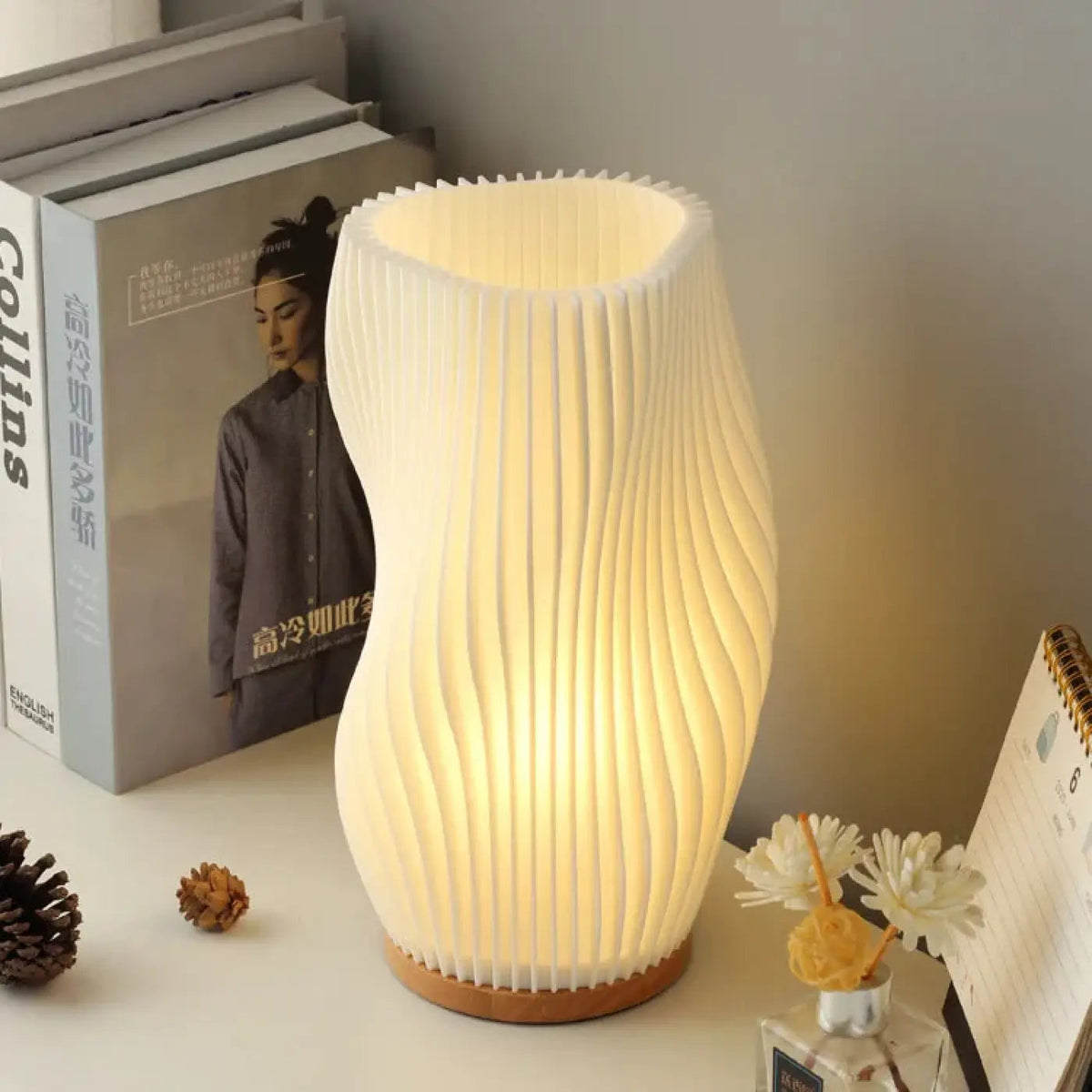Lourna twisted wave pleated table lamp in warm beige glowing on wooden desk with books